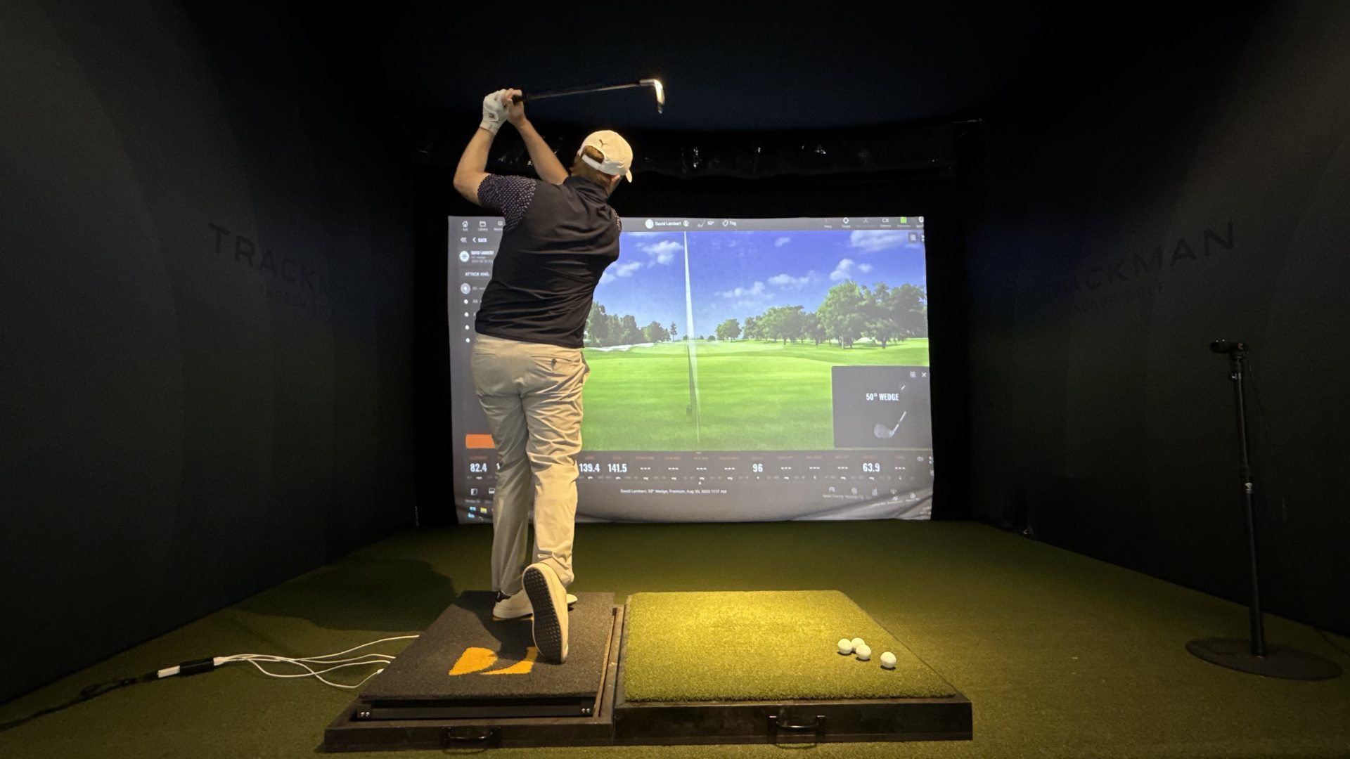 Student swinging on Swing Catalyst force plates with TrackMan data on screen at Dave Lambert Golf studio